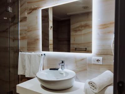 Moderní koupelna se osvětleným zrcadlem, kulatým umyvadlem a bílými ručníky.