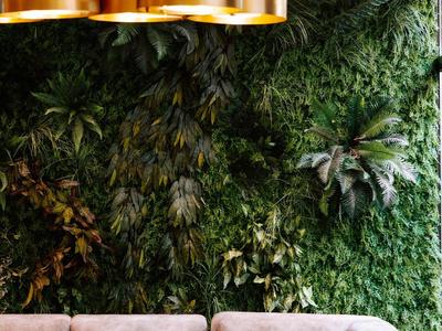 Moderní lounge s hnědým rohovým gaučem a zelenou rostlinnou stěnou v pozadí.