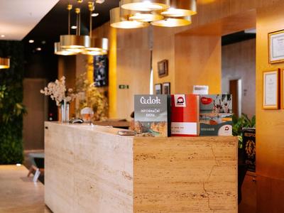 Moderní hotelová recepce se světlým přírodním kamenem a zlatými závěsnými svítidly.