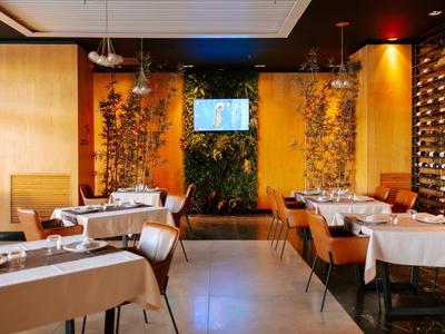 Elegantní restaurace s bílými ubrusy, dřevěnými stěnami a osvětlenou vinotékou.