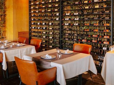 Útulná restaurace s stoly, pohodlnými židlemi a velkým vinným regálem na zdi.