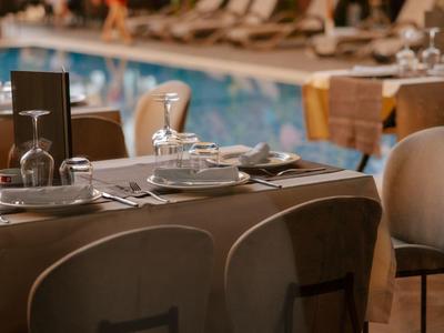 Nastavený stůl se židlemi u bazénu v relaxační venkovní scéně.