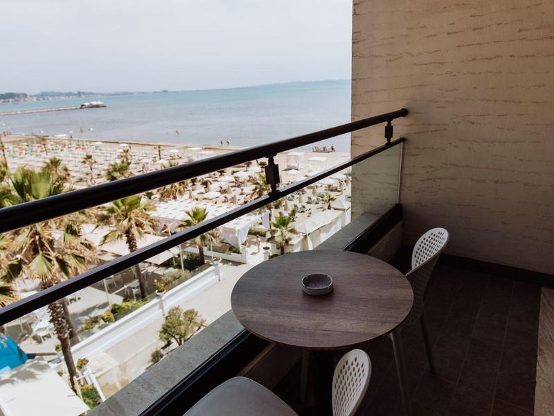 Balkon s malým stolem a židlemi s výhledem na moře a palmy.