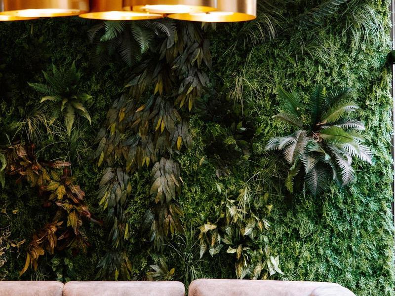 Moderní lounge s hnědým rohovým gaučem a zelenou rostlinnou stěnou v pozadí.