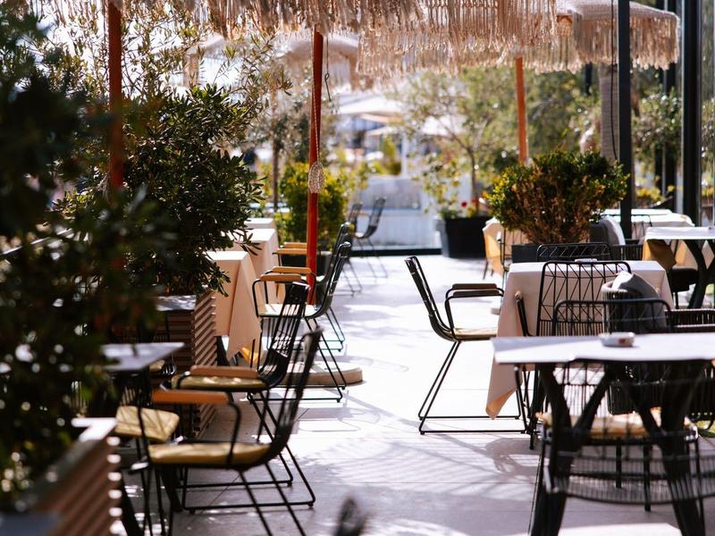 Venkovní terasa s stoly, židlemi a velkými slunečníky vedle hotelové budovy.