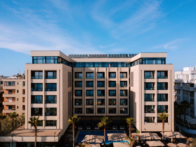 Moderní vícepodlažní hotel s velkým bazénem a palmami v popředí.