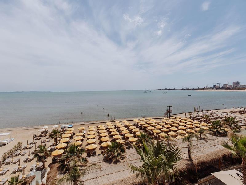 Pláž s mnoha slunečníky a lehátky, klidné moře a zatažená obloha.