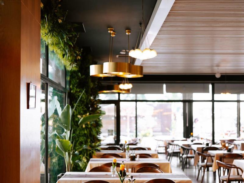 Moderní hotelová restaurace s elegantními zlatými závěsnými světly, dřevěným nábytkem a velkými okny.