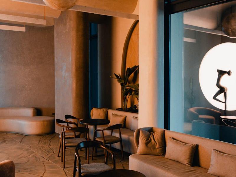 Modern hotel lounge area with sofas, armchairs, and round tables in muted tones.