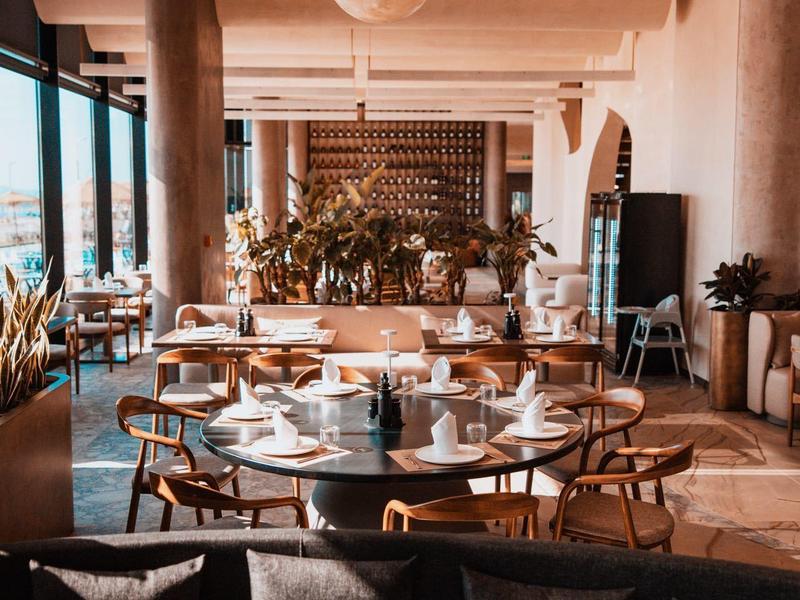 Modern hotel restaurant area with round tables, chairs, and large pendant lights.