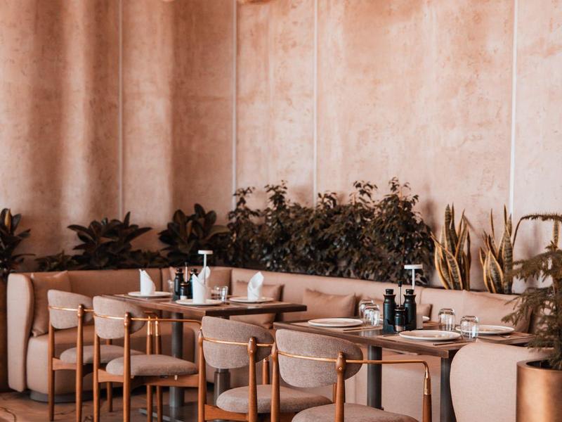 Modern café with round wooden tables, chairs, and hanging globe lights on light walls.
