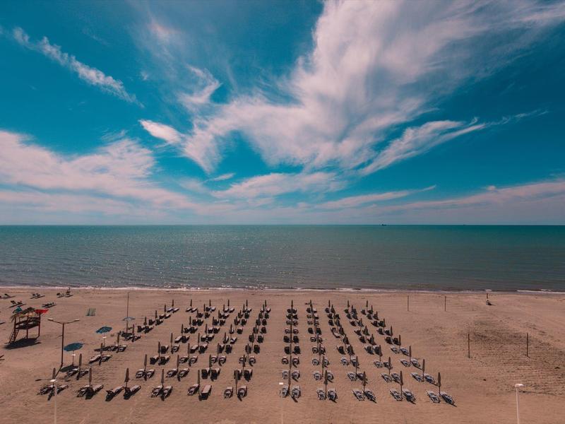 Wide sandy beach with rows of sun loungers and blue sky over the sea.