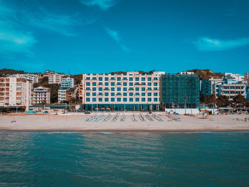 Beach with sun umbrellas in front of multi-story hotels under a blue sky.