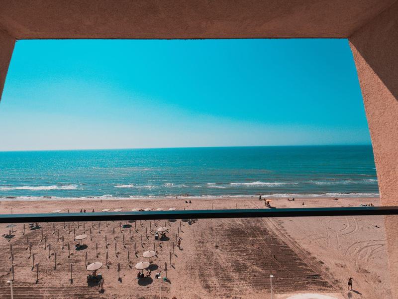 View of sea and beach through a rectangular window in a wall.
