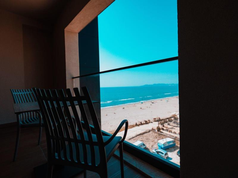 View from a balcony with chairs overlooking a beach and the sea under a clear sky.