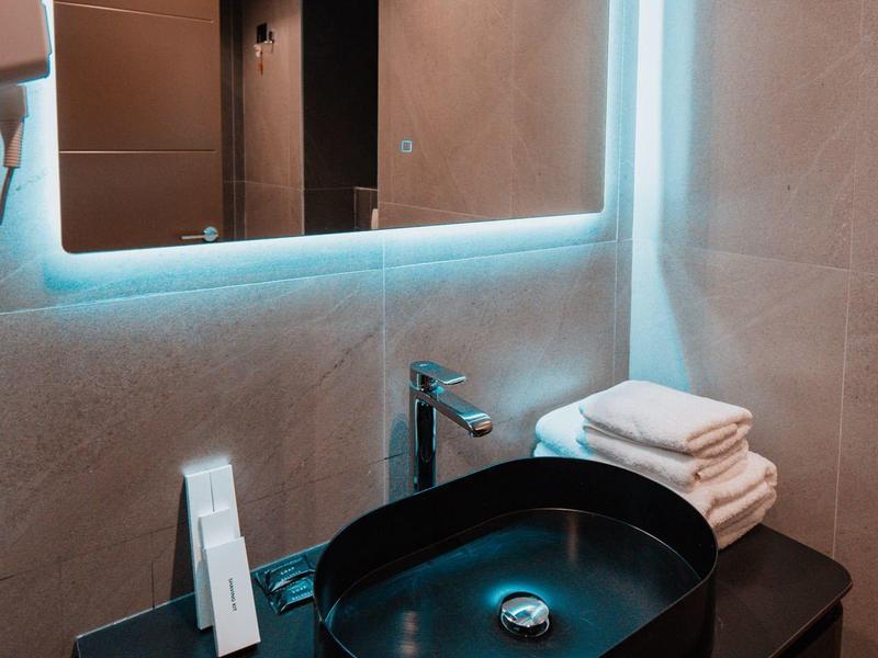 Modern bathroom sink with round black basin and illuminated mirror.