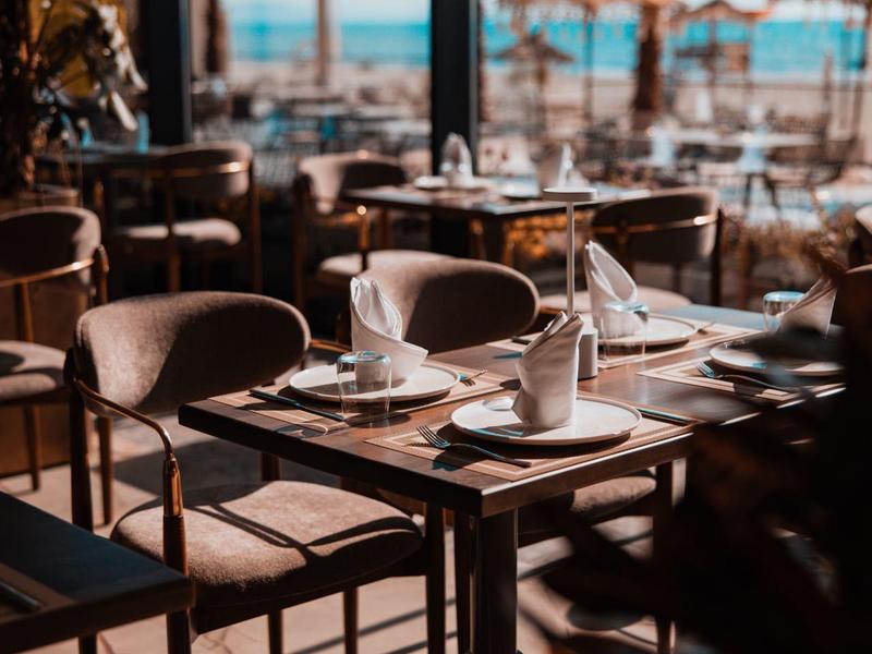 Elegant outdoor restaurant area with set tables and umbrellas by the beach.