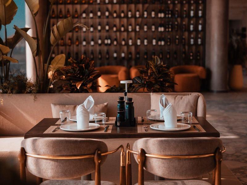 A stylish restaurant with wooden tables, chairs, and a wall full of decorative bottles.
