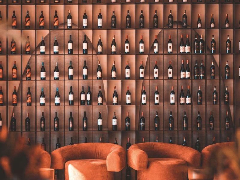 Modern lounge area with orange chairs in front of a wall filled with wine bottles.