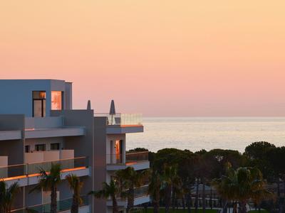 Moderne Gebäude mit Balkonen, Palmen im Vordergrund und ruhiger Meereshorizont bei Sonnenuntergang.
