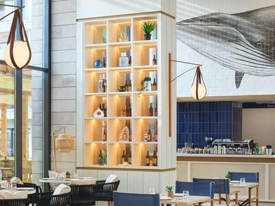 Helles Café mit Holzregalen, blauen Stühlen und großem Kunstwerk an der Wand.