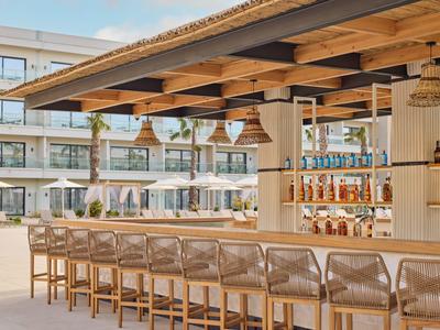 Moderner Außenbarbereich mit Holzdach, hohen Barhockern und Regalen voller Flaschen.