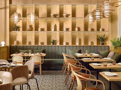 Modernes, warm beleuchtetes Restaurant mit Holzwänden, Pflanzen und gedeckten Tischen in hellem Holz.