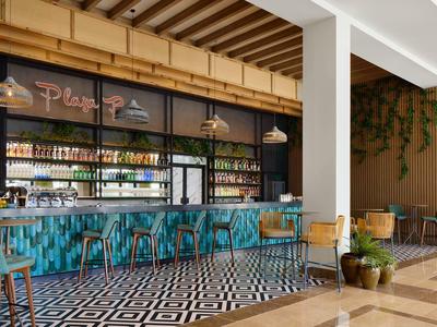 Moderner Barbereich mit türkisfarbenen Sitzhockern, Holzdecke und schwarz-weiß gemustertem Boden.