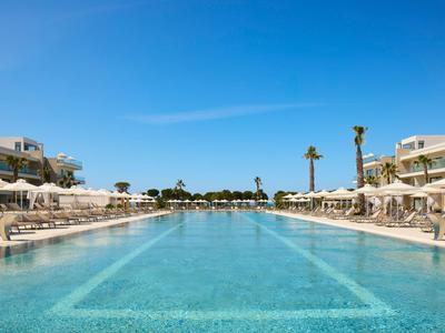 Großer Außenpool mit Sonnenliegen und weißen Sonnenschirmen in einem Hotelresort bei sonnigem Himmel.