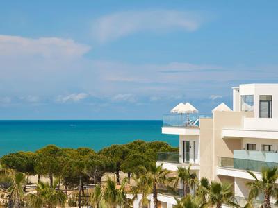Blick auf blaues Meer, grünen Wald und weiße moderne Gebäude unter klarem Himmel.