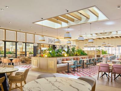 Moderner, heller Gastraum mit Holz-, Marmor- und Pastellfarben, großer Pflanzeninsel und viel Tageslicht.