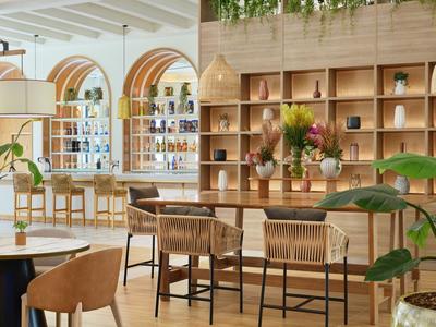 Modern eingerichtete Bar mit Holztheke, Hockern und großen Fenstern in einem Hotel.