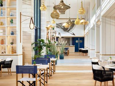 Modernes, helles Restaurant mit Holzfußboden, goldenen Pendelleuchten und blauen Stühlen.