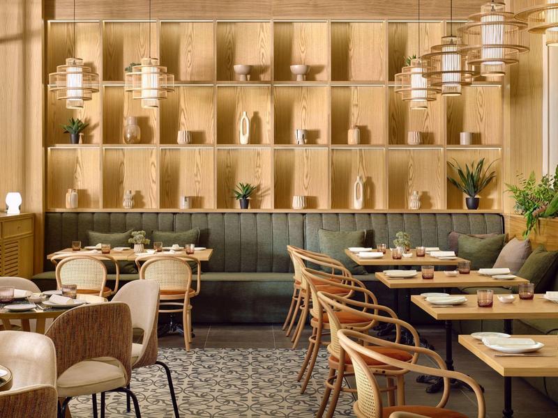 Modernes, warm beleuchtetes Restaurant mit Holzwänden, Pflanzen und gedeckten Tischen in hellem Holz.