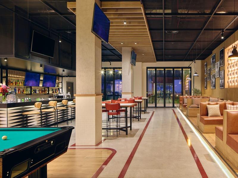 Moderner Barraum mit Billardtisch, Theke, hohen Tischen und Ledersesseln in warmen Farben.