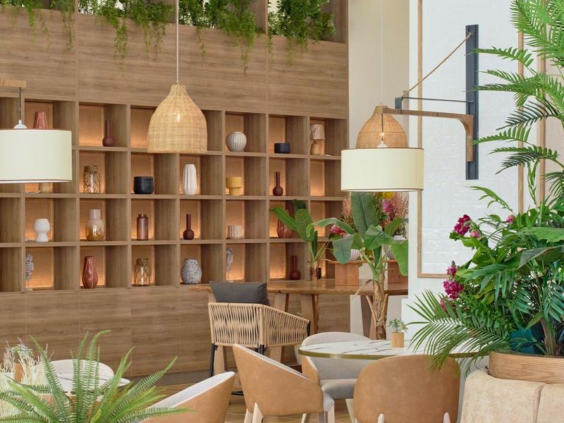 Helles, modernes Café mit Holzregalen, Pflanzen und bequemen Sitzgelegenheiten in natürlicher Farbgebung.