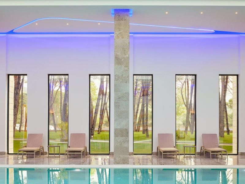 Moderner Innenpool mit großen schmalen Fenstern, grauem Pfeiler und blauer LED-Beleuchtung.