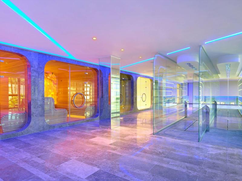 Moderner Raum mit farbig beleuchteten Glaswänden und reflektierendem Boden in Blau und Orange.