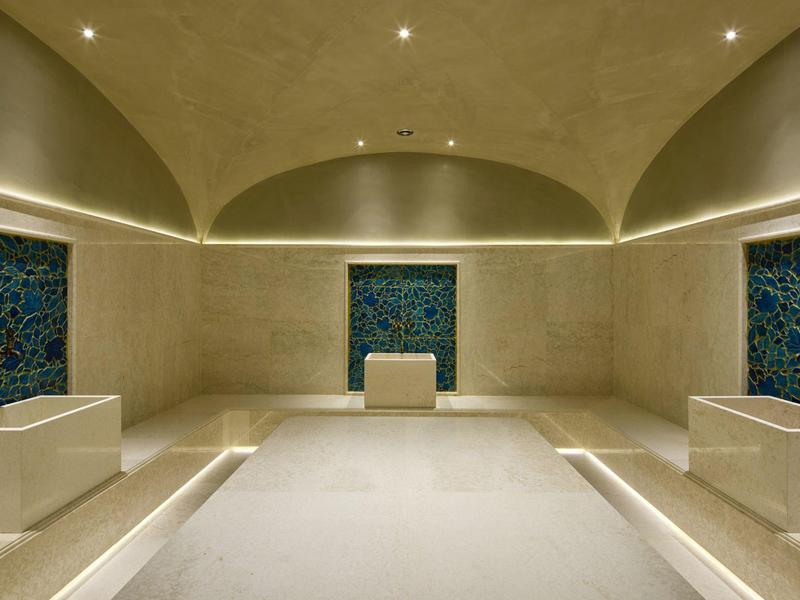 Moderner Spa-Raum mit beiger Marmorverkleidung, drei Nischen und indirekter Beleuchtung.