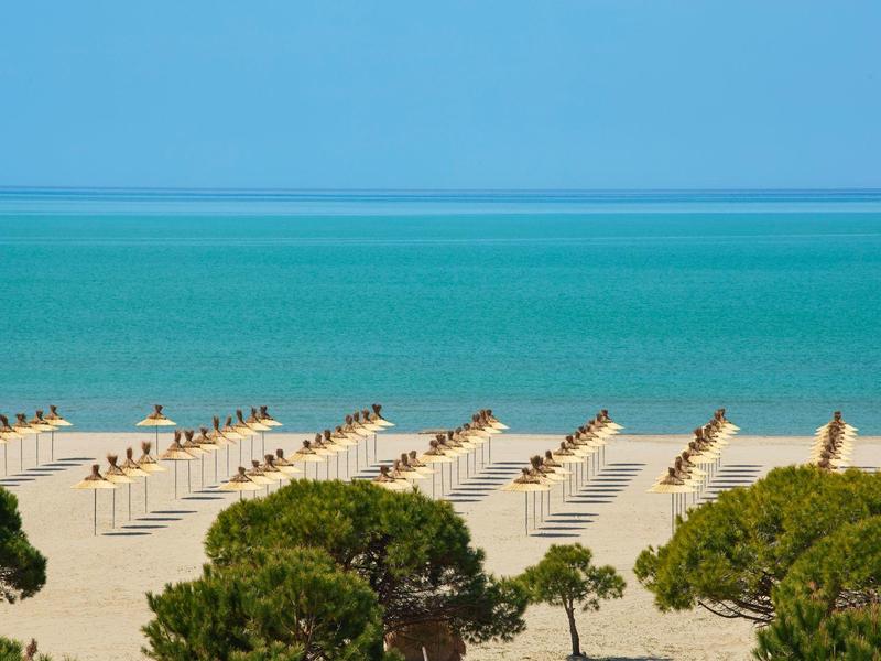 Strand mit Reihen leerer Sonnenschirme, türkisfarbenes Meer und blauer Himmel im Hintergrund.