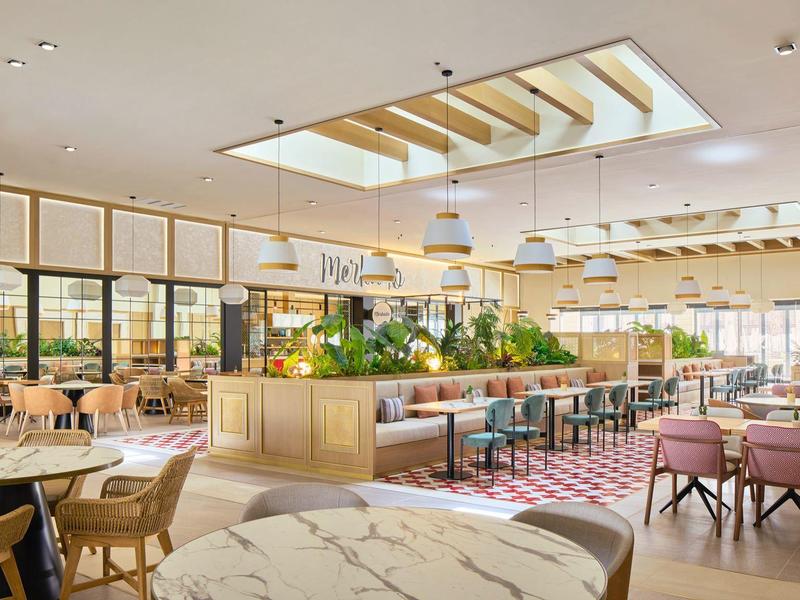 Moderner, heller Gastraum mit Holz-, Marmor- und Pastellfarben, großer Pflanzeninsel und viel Tageslicht.