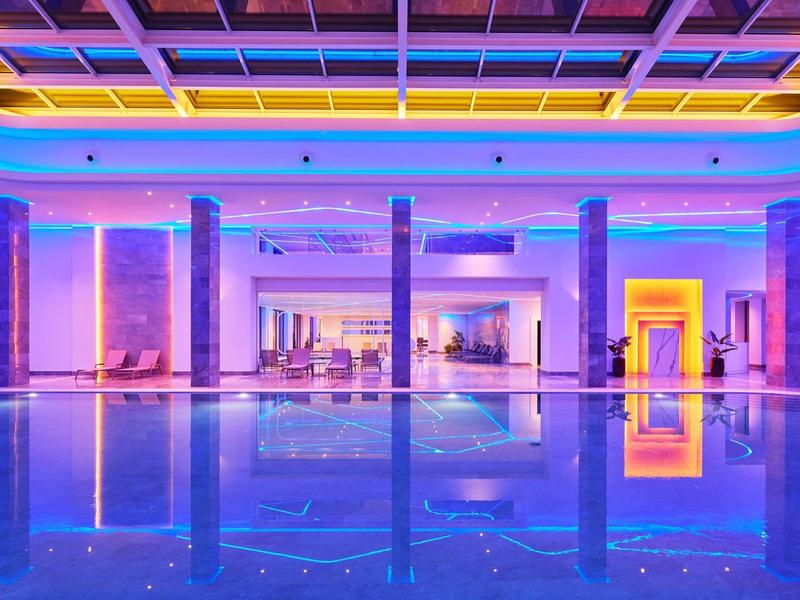 Innenraum eines modernen Pools mit blau-lila Beleuchtung und reflektierendem Wasser.