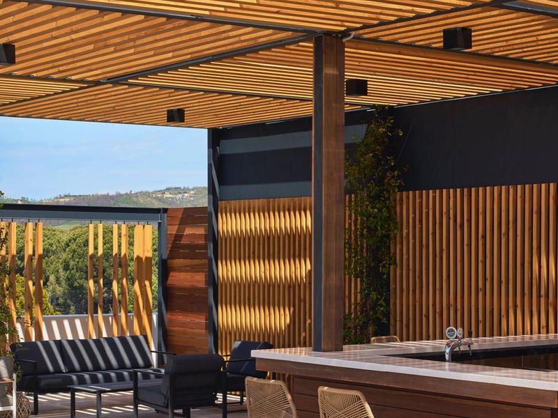 Moderne Terrasse mit Holzlamellendach, Lounge-Möbeln und Bar aus Holz, Naturfarben und klarem Himmel.