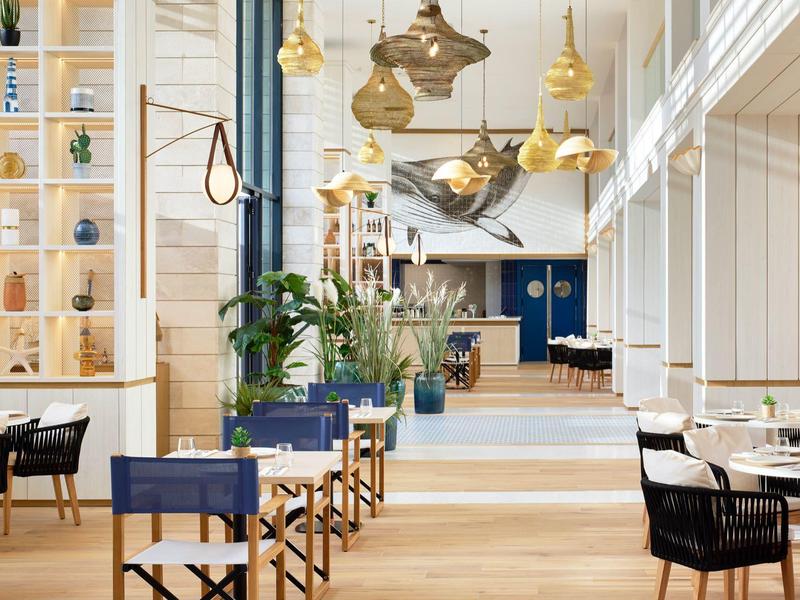 Modernes, helles Restaurant mit Holzfußboden, goldenen Pendelleuchten und blauen Stühlen.