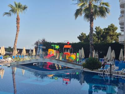 Swimming pool with two palm trees, water park, and many sun loungers under clear sky.