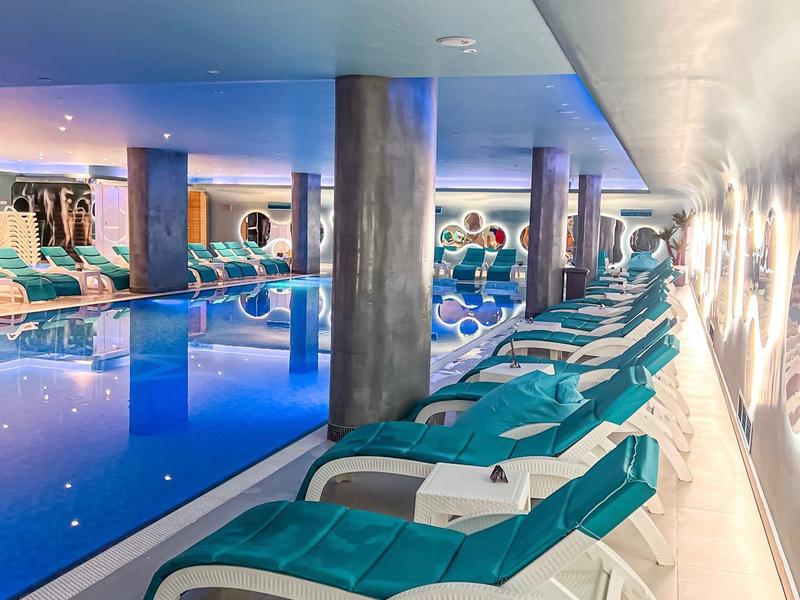 Indoor pool with blue loungers and illuminated water in a modern hotel.