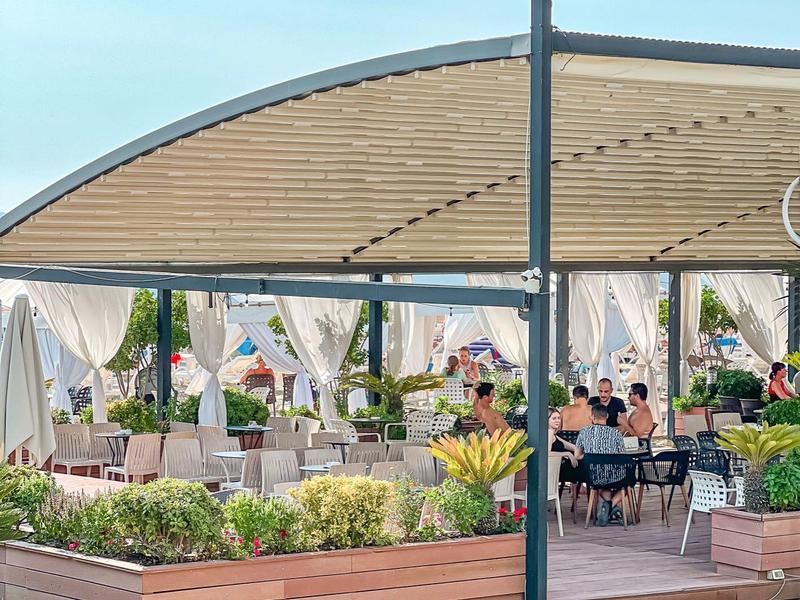 Covered outdoor restaurant area with seating and plants in wooden planters.
