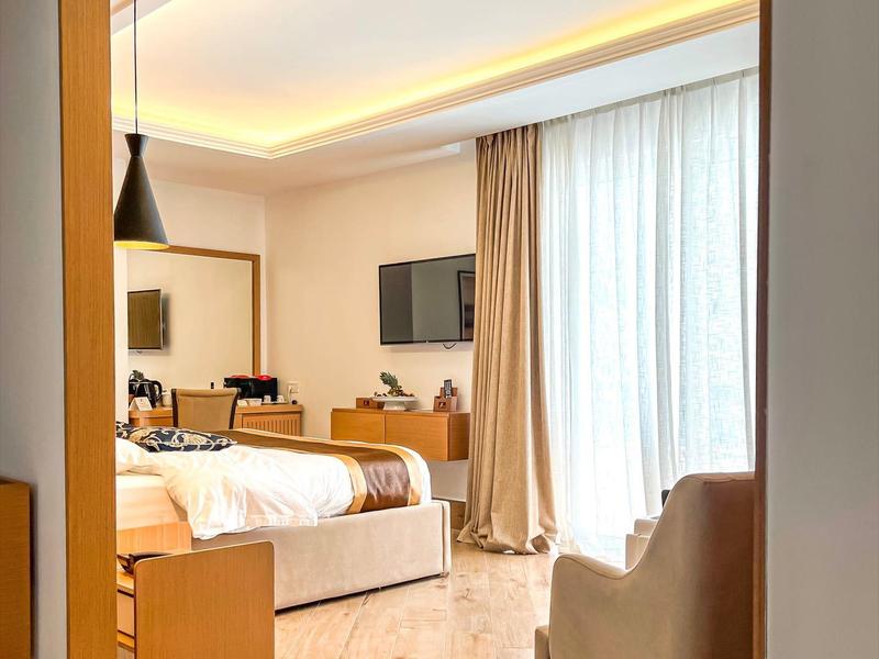 Modern hotel room with wooden floor, large bed, and floor-to-ceiling windows.