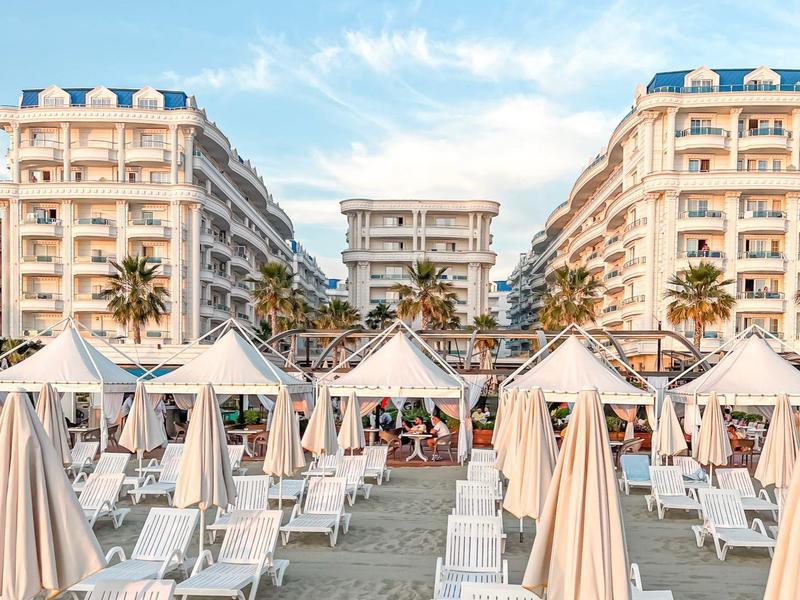 Sandy beach with white lounge chairs and umbrellas between large hotels.