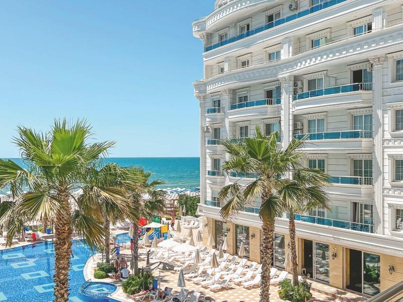 Modern hotel pool with palm trees in front of a multi-story hotel building by the sea.